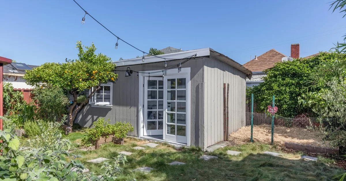 A gray dwelling unit with white doors. String lights extend outward from the unit and various plants surround the space.