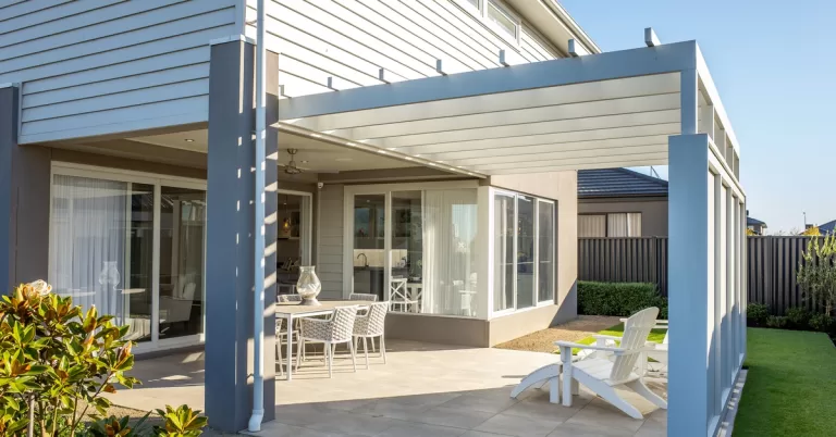 A white pergola stands over beige tile flooring with white outdoor furniture arranged beneath it.