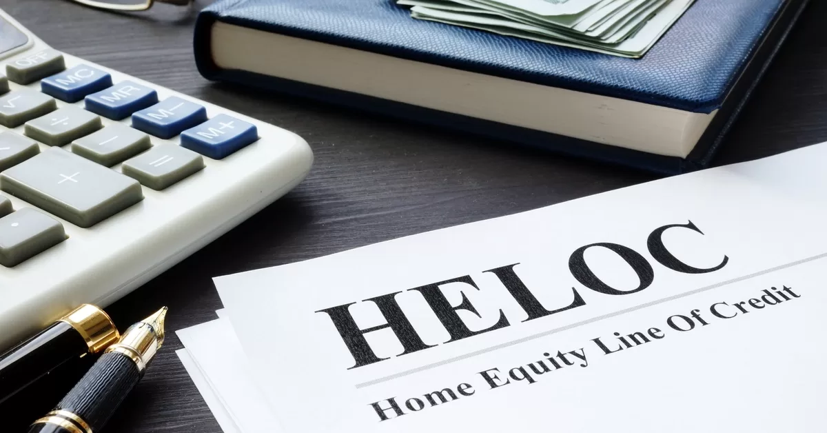 A sheet labeled "HELOC" and "Home Equity Line of Credit" lies beside a pen, calculator, glasses, journal, and cash.