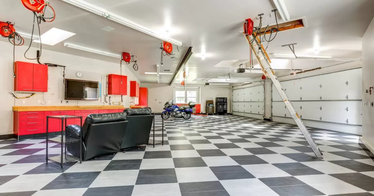 A spacious garage shows two closed white doors, black-and-white checkerboard flooring, recliners, and red cabinets.