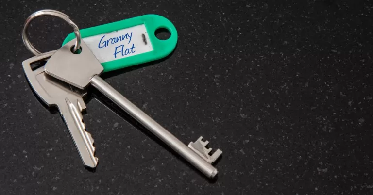 Two silver keys and a green key tag with “Granny Flat” written in blue pen sit on a black marbled surface.