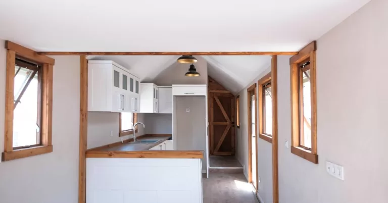 White walls and ceiling surround wood-trimmed windows and a doorway. Two black pendant lights hang above wood counters.