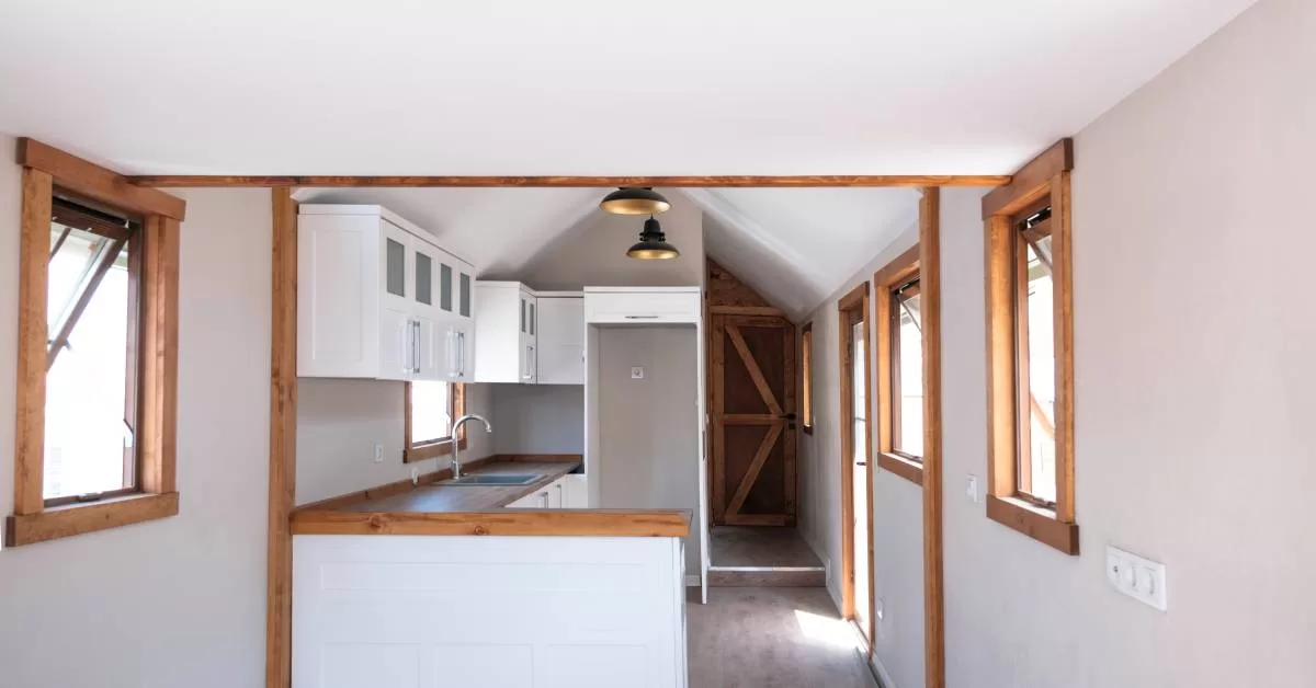 White walls and ceiling surround wood-trimmed windows and a doorway. Two black pendant lights hang above wood counters.