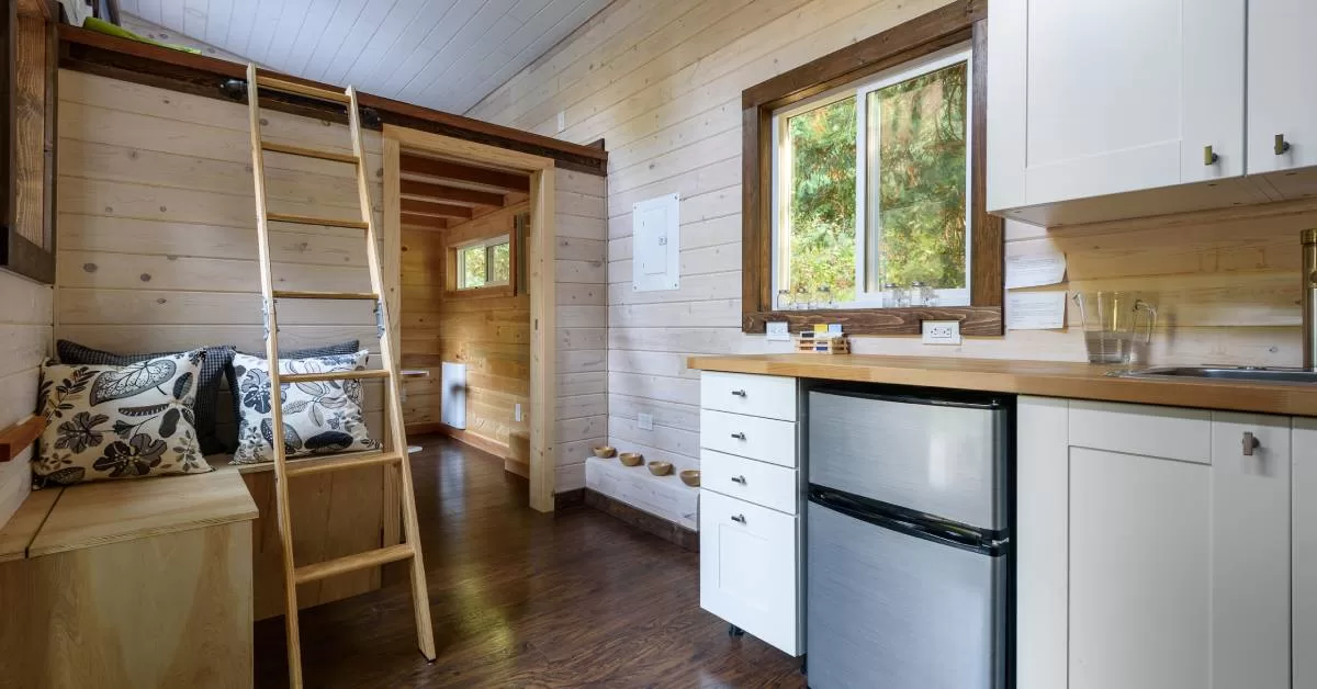 A wood-paneled interior features white cabinetry, a wooden bench with pillows, and a ladder leading to a lofted area.