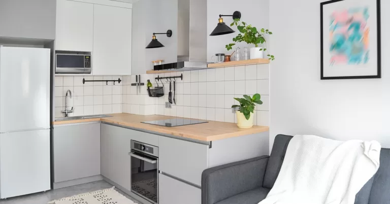 A gray couch sits near white and gray cabinets, a countertop with a stovetop, a microwave, and a range hood.