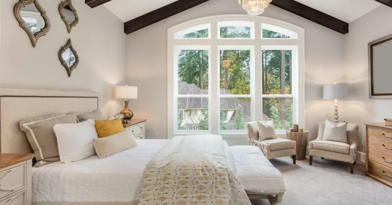 A beautifully furnished primary bedroom has a vaulted ceiling with a gorgeous chandelier hanging from it.