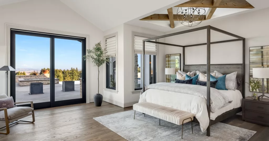 A new primary suite addition in a home has doors opening to a balcony and a modern sky light above the bed.