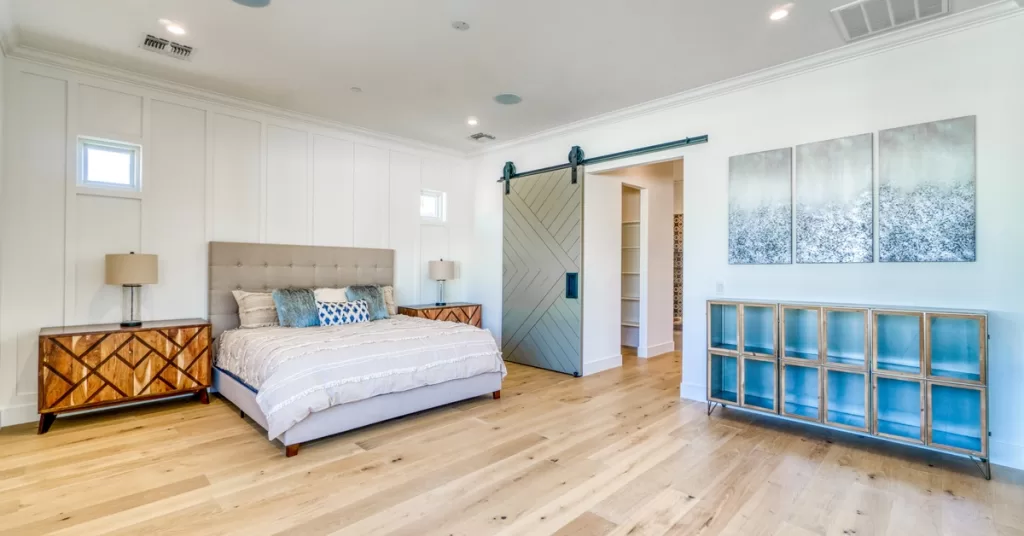 A primary suite addition in a home has a sliding barn door with new lightly colored hardwood floors.
