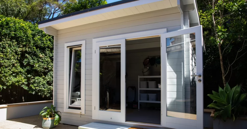 A tiny room or in-law suite in the corner of a property. It's sunny and the door and window are both open.