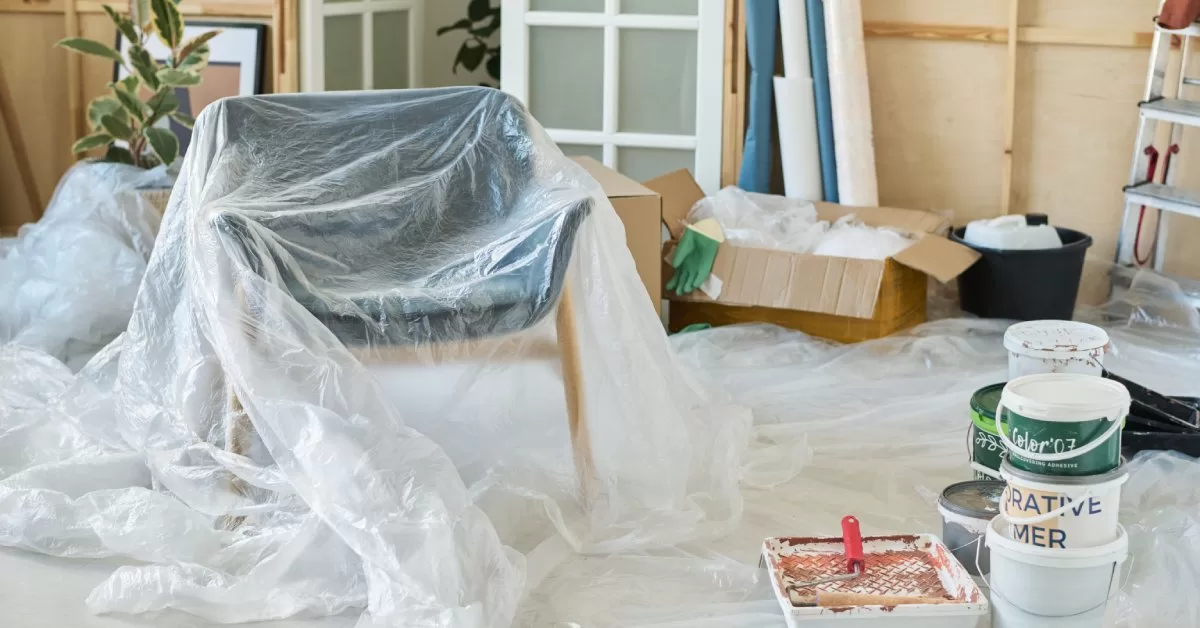 A room contains furniture and belongings covered by a plastic tarp to protect it during a renovation.