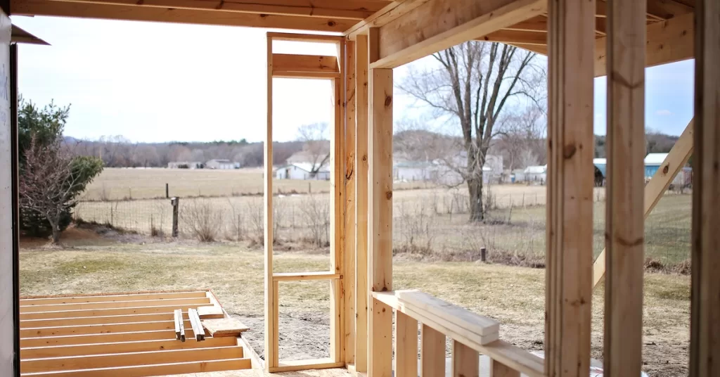 Wood framing of a new home addition. The structure is exposed to the outdoors with a field behind the home.