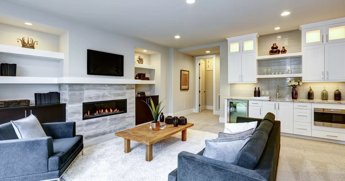 A modern living room contains a fireplace, TV, dark furniture, and a wet bar featuring white cabinets and a beverage fridge.