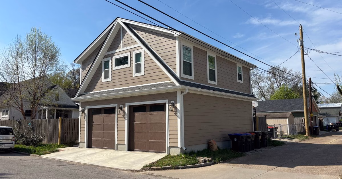 Two-story detached garage with beige siding, white trim, dual garage doors, and upper-level living space on a residential alley.