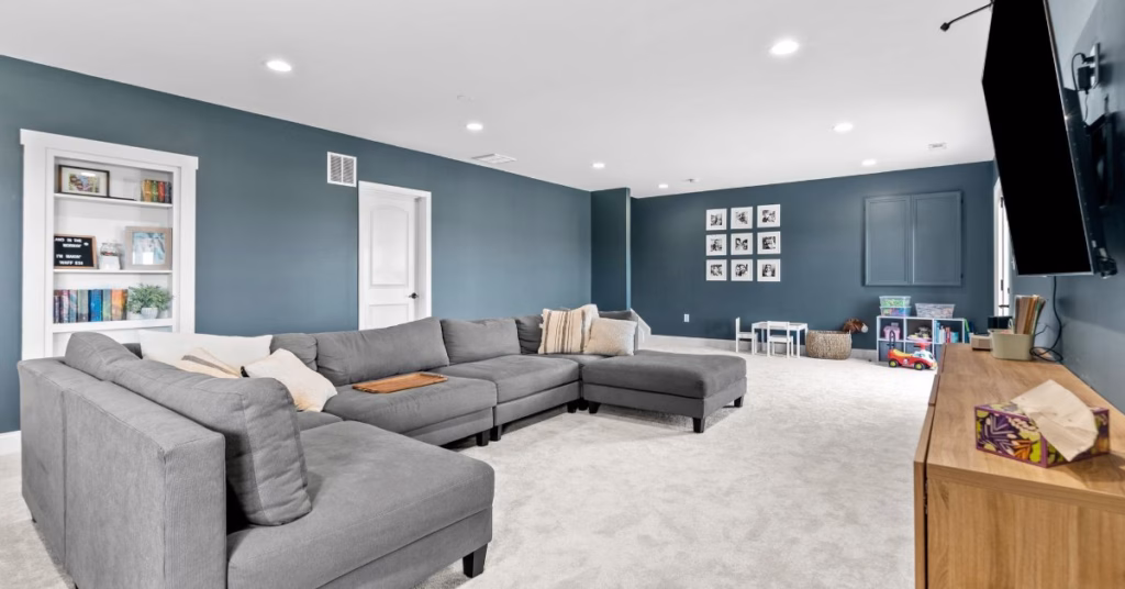 A spacious living room featuring sectional sofas, blue accent walls, recessed lighting, and wall decor.