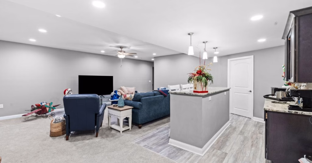 A finished basement opens into a spacious lounge with blue seating, a wet bar, and bright recessed lighting
