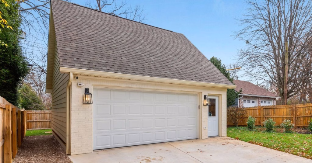 A detached two-car garage with a steep roof, white door, and side entry stands inside a fenced yard.