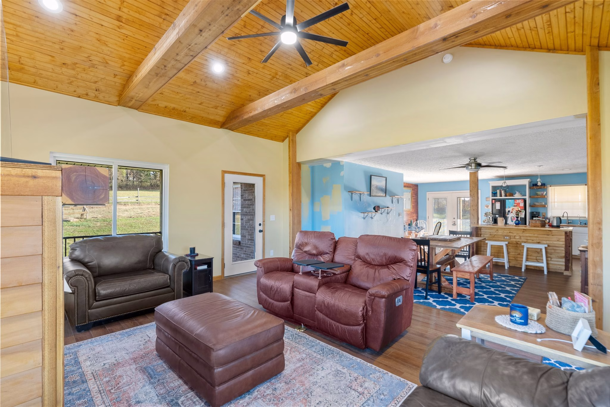 An open living room features a vaulted wood ceiling with exposed beams, leather seating, and a view into a dining area.